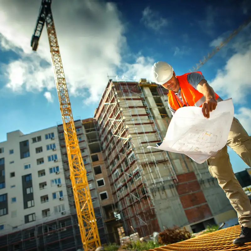 Engenheiro de capacete analisando um projeto em frente a um prédio em obras